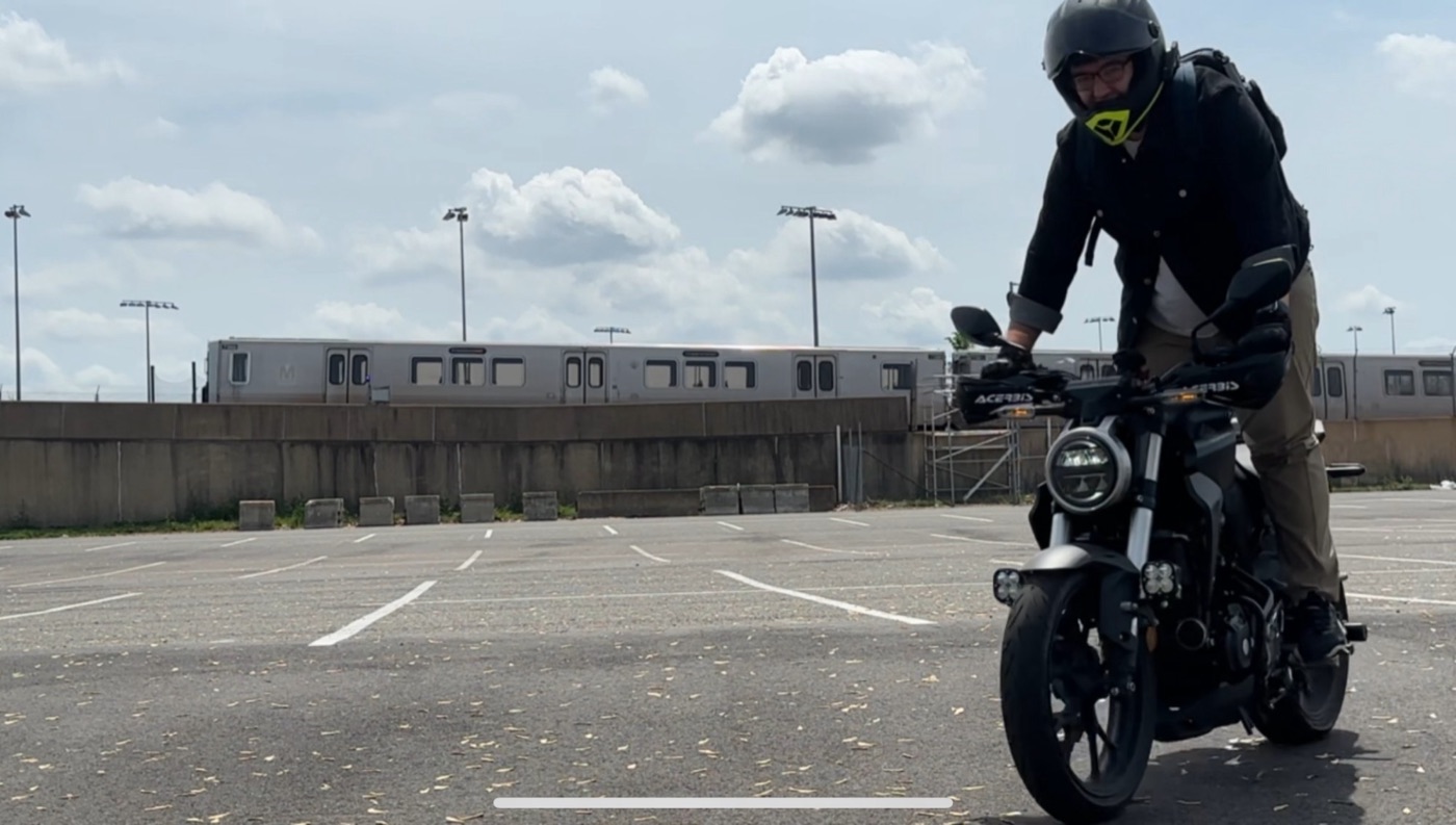 Alexander on his Honda CB300R in a parking lot, with a Metro train behind him.