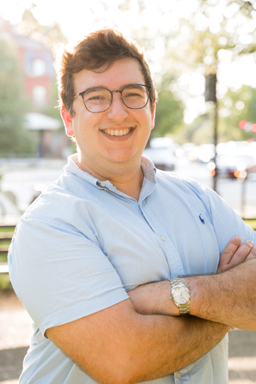 Portrait of Alexander Kaufman, smiling outdoors, arms crossed.